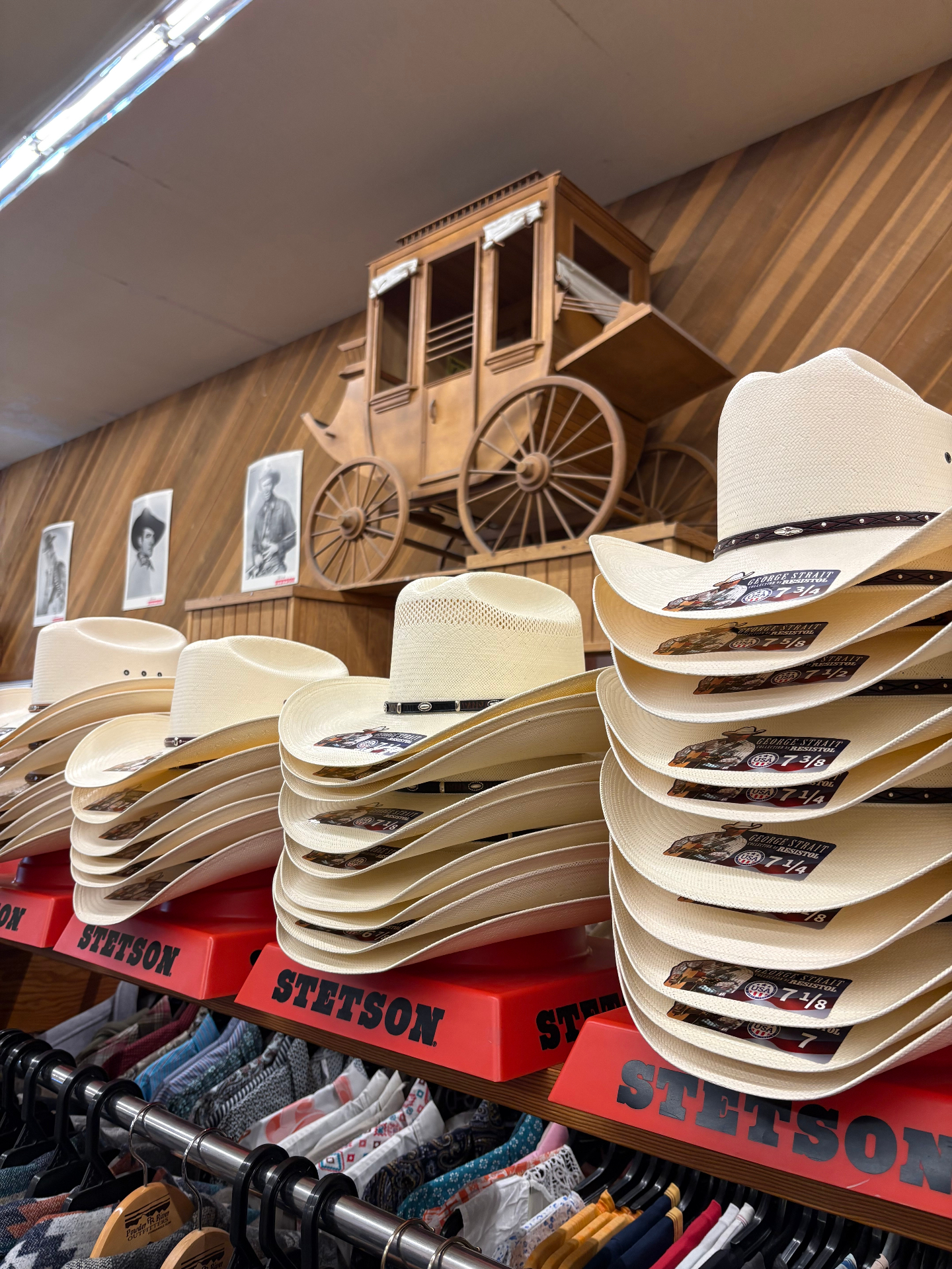 Stacks of Stetson straw hats with a model stagecoach and vintage cowboy portraits behind